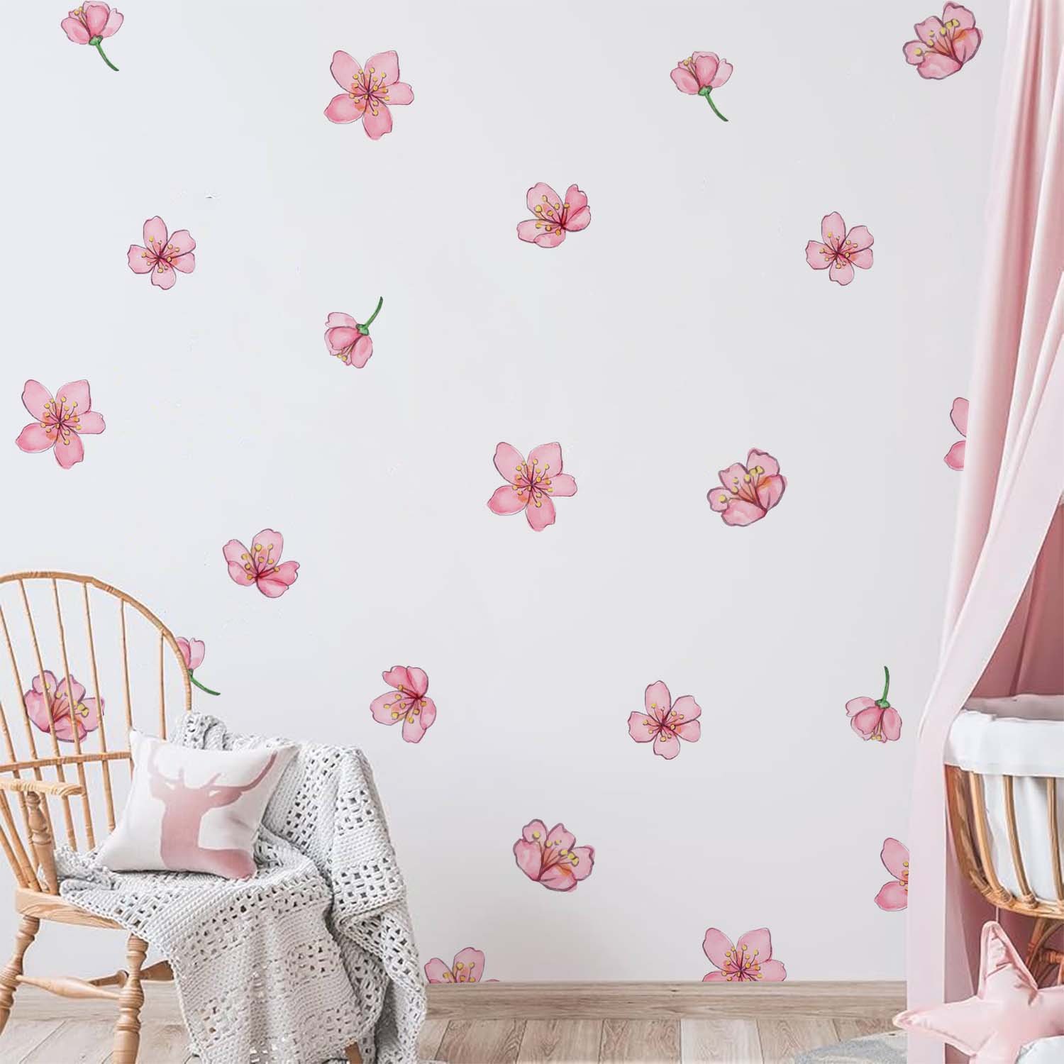 Scattered pink cherry blossom wall stickers decorating a soft pastel nursery wall beside a wicker chair, knitted blanket, and pink canopy crib.