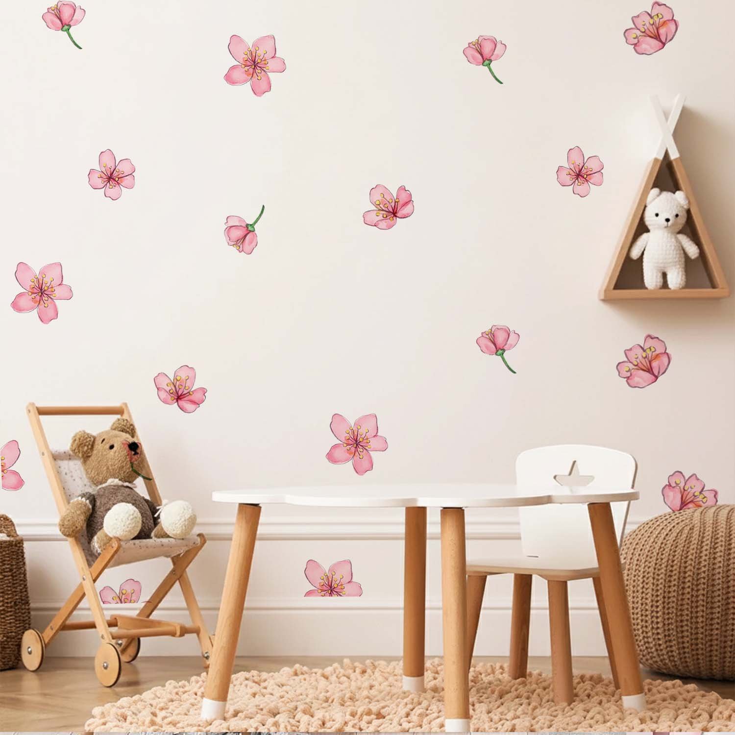 Scattered pink cherry blossom wall stickers decorating a soft pastel nursery wall beside a wicker chair, knitted blanket, and pink canopy crib.