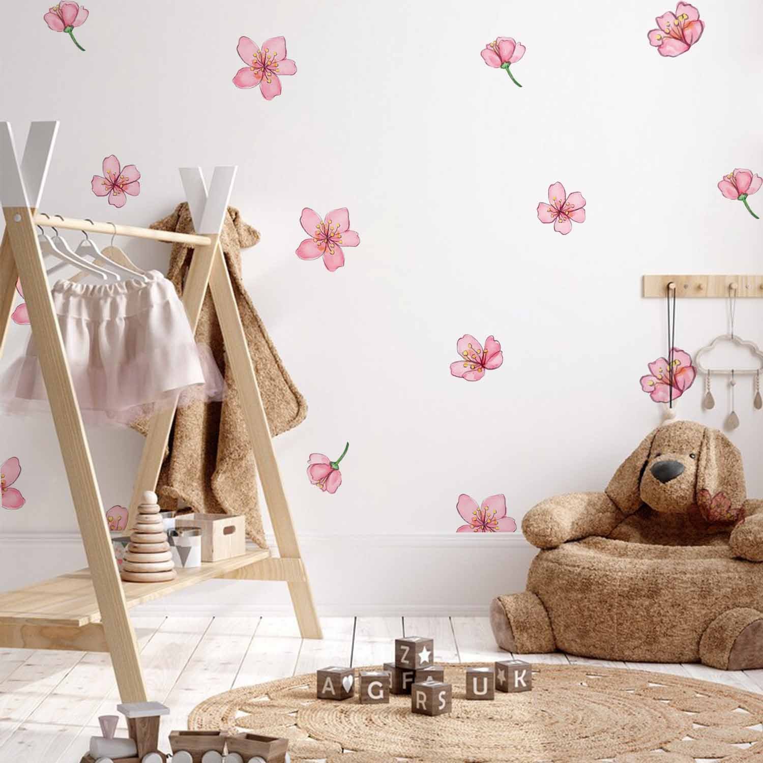 Scattered pink cherry blossom wall stickers decorating a soft pastel nursery wall beside a wicker chair, knitted blanket, and pink canopy crib.