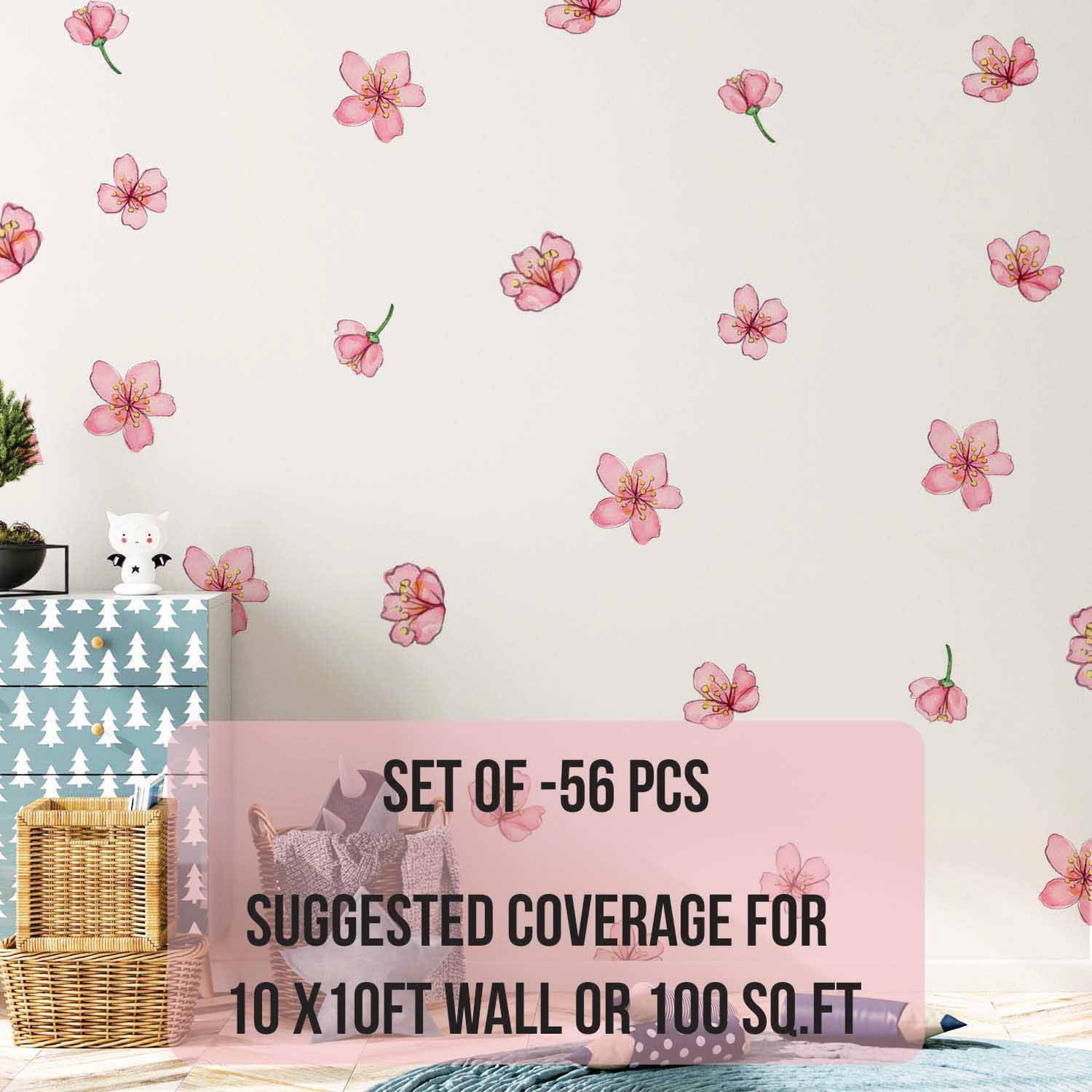 Scattered pink cherry blossom wall stickers decorating a soft pastel nursery wall beside a wicker chair, knitted blanket, and pink canopy crib.