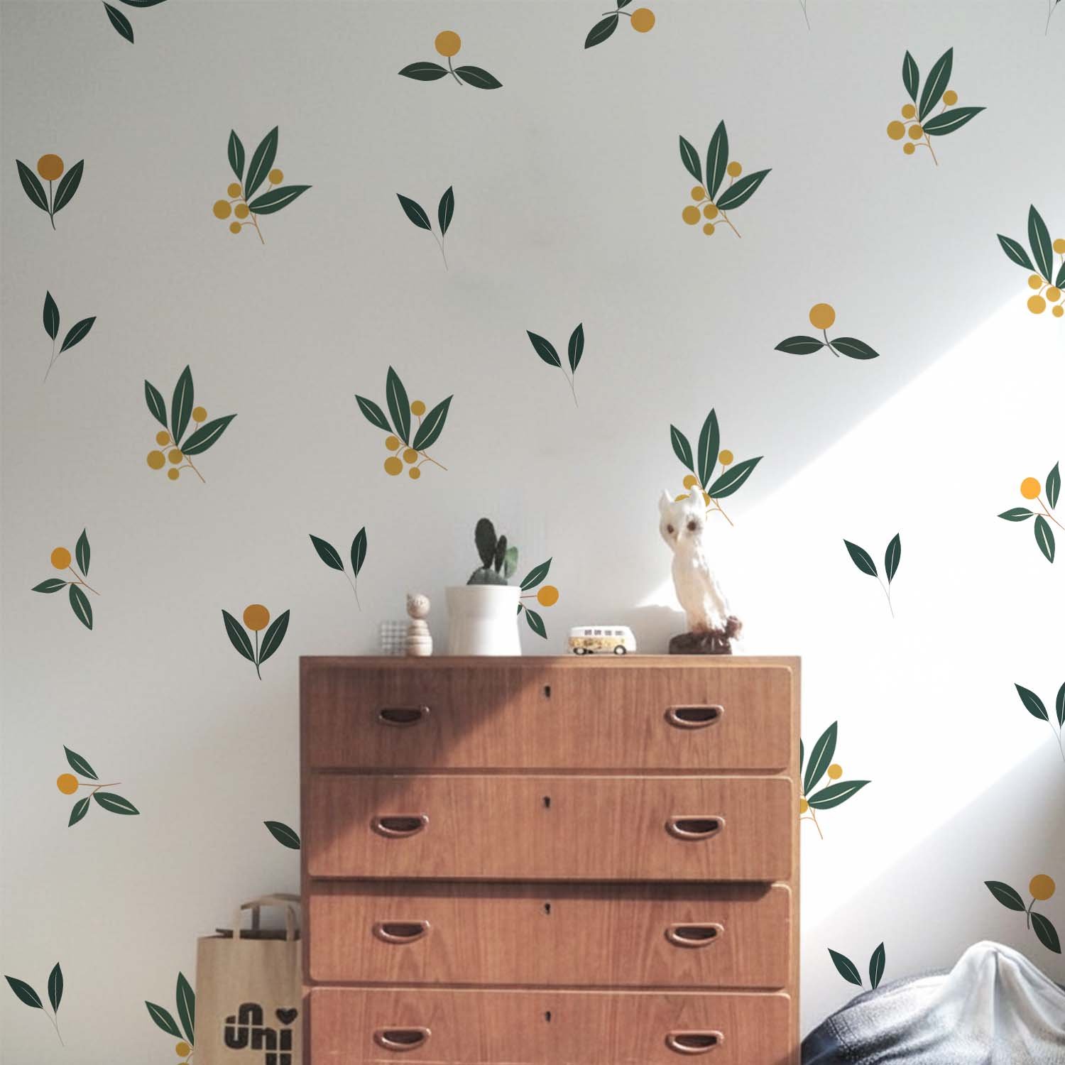 Minimalist botanical wall stickers featuring green leaves and yellow berry motifs arranged in a scattered pattern above a beige sofa in a modern living room.