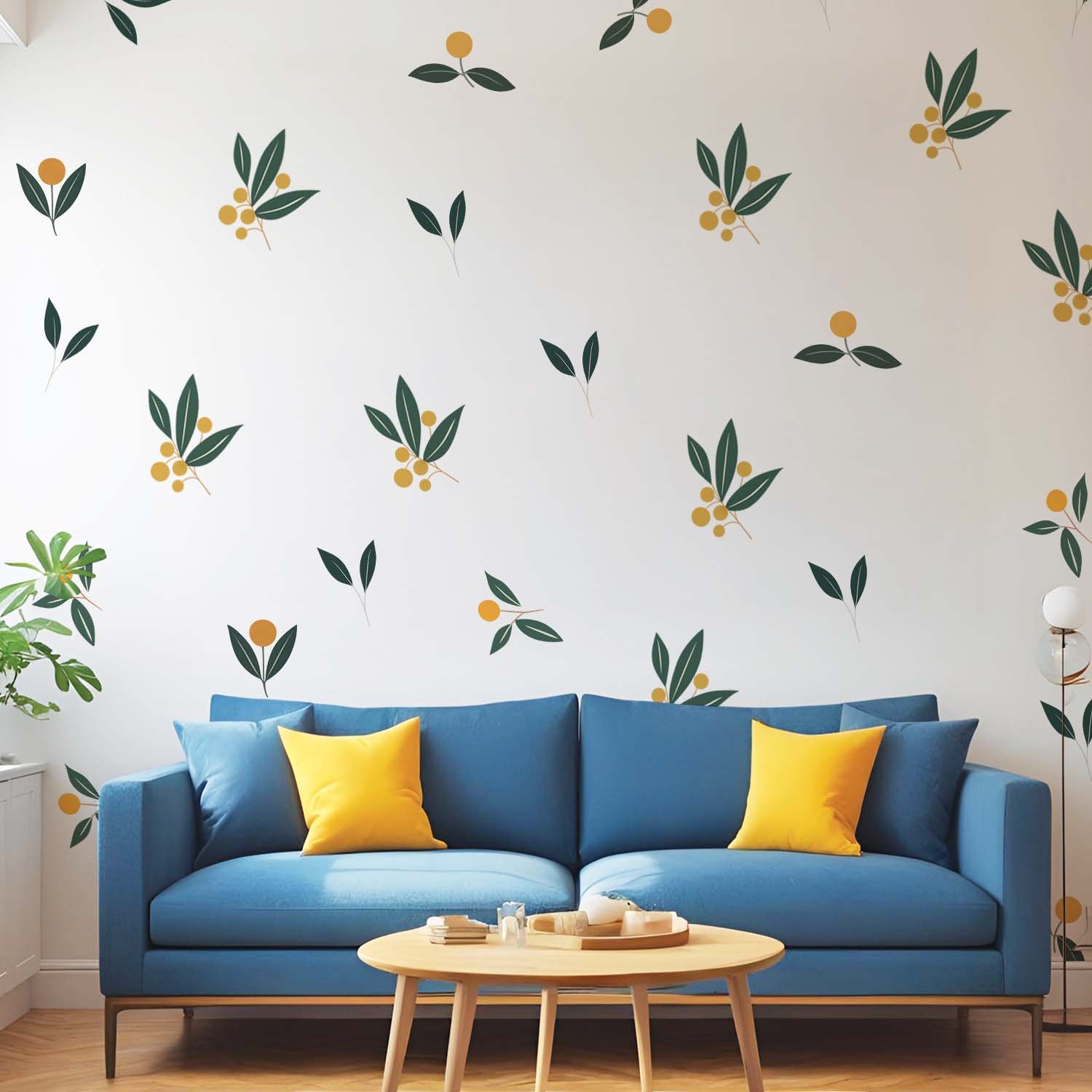 Minimalist botanical wall stickers featuring green leaves and yellow berry motifs arranged in a scattered pattern above a beige sofa in a modern living room.