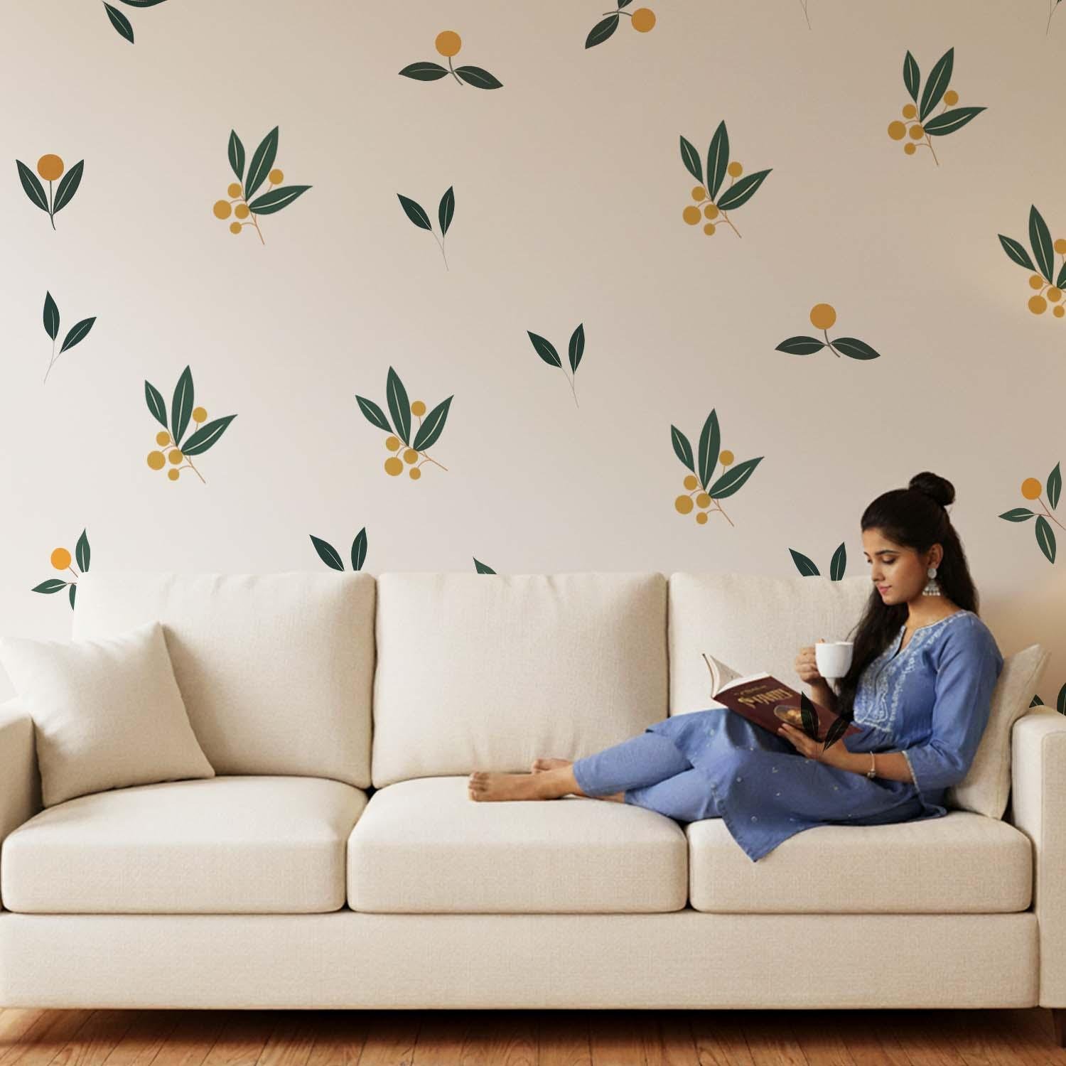 Minimalist botanical wall stickers featuring green leaves and yellow berry motifs arranged in a scattered pattern above a beige sofa in a modern living room.