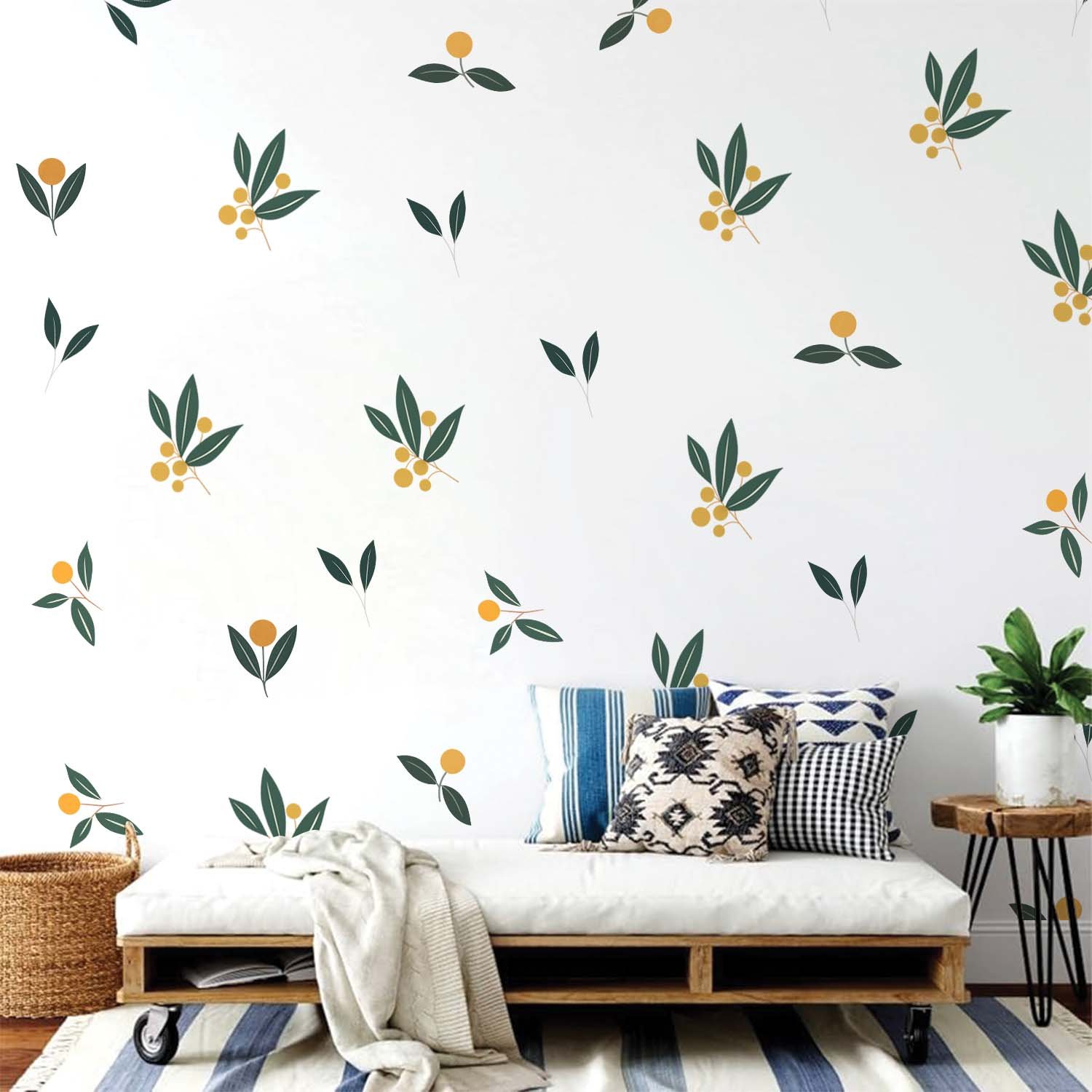 Minimalist botanical wall stickers featuring green leaves and yellow berry motifs arranged in a scattered pattern above a beige sofa in a modern living room.