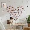 A children's bedroom featuring pink, brown, and mauve heart wall stickers arranged in a large heart shape above a wooden bench, creating a cozy boho nursery decor theme.