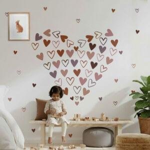 A children's bedroom featuring pink, brown, and mauve heart wall stickers arranged in a large heart shape above a wooden bench, creating a cozy boho nursery decor theme.