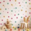 A nursery featuring pastel pink, blue, and lavender daisy wall stickers scattered across a white wall above a baby crib with plush toys.